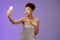 Stylish silly feminine african-american woman partying in silver stylish dress folding lips mwah gesture posing selfie