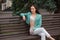 A stylish slender smiling woman sits on a bench under a Christmas tree, on a street in the city