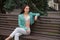 A stylish slender smiling woman sits on a bench under a Christmas tree, on a street in the city