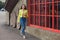 A stylish slender smiling woman walks near a building with wooden red windows, along a street in the city