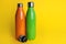 Stylish stainless thermo bottles on yellow background. Space for text