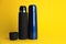 Stylish stainless thermo bottles on yellow background. Space for text