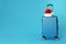 Stylish suitcase with Santa Claus hat on background, space for text. Christmas vacation