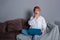 Stylish Surprised woman with laptop in hands on sofa and looking at laptop . Dressed in a white shirt and jeans with embroidery