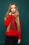 Stylish teen, beautiful young model girl with long blonde hair, posing at studio in jeans and red sweatshirt