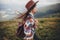 Stylish traveler girl in hat with backpack walking in mountains.