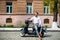 Stylish trendy man wearing modern sunglasses and a formal suit sitting waiting on a motorcycle on city street