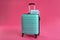 Stylish turquoise suitcase and protective masks with inscription COVID-19 on pink background.