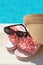 Stylish visor cap, slippers and sunglasses near outdoor swimming pool on sunny day, closeup