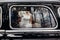 Stylish wedding couple sitting in beautiful black car, creative view from window. elegant groom and bride walking and holding