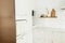 Stylish white kitchen cabinets with brass knobs, wooden shelves with utensils and appliances in new scandinavian house. Modern