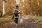 Stylish woman with backpack hiking with white dog in sunny autumn woods. Cute swiss shepherd puppy