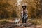 Stylish woman with backpack hiking with white dog in sunny autumn woods. Cute swiss shepherd puppy