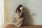 Stylish woman in cozy knitted sweater posing with chrysanthemum on background of rural authentic wall. Moody fall. Young