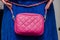 stylish woman of fashionable woman has a small quilted pink leather bag (clutch) on the background of a bright blue (electric) dr