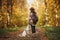 Stylish woman in hat with backpack standing with cute dog in sunny autumn woods. Young female hipster traveling with swiss