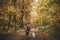 Stylish woman in hat and with backpack walking with cute dog in sunny autumn woods. Young female traveler hiking with swiss