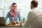 Stylish woman in hijab making conversation at desk with man