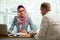 Stylish woman in hijab making conversation at desk with man