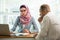 Stylish woman in hijab making conversation at desk with man