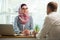 Stylish woman in hijab making conversation at desk with man