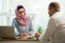 Stylish woman in hijab making conversation at desk with man