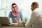 Stylish woman in hijab making conversation at desk with man