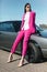 Stylish woman in a pink suit waiting near classic car