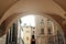 Stylish woman standing in sunlight under arch of old building tu