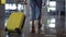 Stylish woman walk with trolley yellow case by empty airport, low half view of slender female legs and medium wheeled