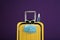 Stylish yellow suitcase with protective mask, sunglasses and antiseptic spray on purple background. Travelling during coronavirus