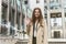 Stylish young businesswoman wearing smart outfit stands in the middle of the street looking gorgeous waving her friend, style and