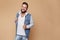 Stylish young cheerful guy with a beautiful beard in a denim jacket and white t-shirt on a plain cream background. Denim jacket