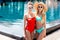 stylish young embracing women in vintage sunglasses standing at poolside and looking