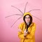 Stylish young girl in a yellow raincoat with a hood on her head with glasses under an umbrella, snuggles into her hands because of