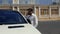 Stylish young man with a beard in a white shirt and dark glasses stands near his white car and speaks on the phone. 4k. 4k video