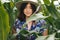 Stylish young woman in blue vintage dress and hat posing in green corn field. Sensual portrait of beautiful girl in cornfield maze