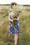 Stylish young woman in blue vintage dress and hat walking with white wildflowers in summer meadow. Happy beautiful girl smiling