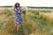 Stylish young woman in blue vintage dress and hat walking with white wildflowers in summer meadow. Happy beautiful girl smiling