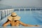 Stylish young woman in hat relaxing in pool and enjoying summer holiday. Back of girl in sunhat on vacation in luxury tropical