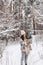 Stylish young woman in a hat stands in a snowy forest with branches of fir nobilis