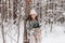 A stylish young woman in a hat stands in a snowy forest with branches of a nobilis fir near a tree.