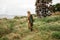 Stylish young woman in khaki shirt walking in steppie, traveling in Africa on safari, wearing hat and brown backpack