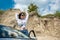 stylish young woman pauses in travel and rests by the roadside near car