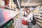 A stylish young woman with a red shopping basket in her hands selects canned vegetables in a supermarket