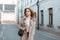 Stylish young woman in a spring light coat in a white T-shirt with a stylish black leather handbag walking down the street