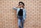 Stylish young woman wearing a black round hat, jeans jacket, female model looking away on brick wall