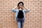 Stylish young woman wearing a black round hat, jeans jacket, female model looking away on brick wall