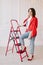 stylish young woman in white t shirt, jeans and red jacket and shoes on high heels is sitting on red ladder. studio