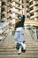 Stylishly dressed woman in blue denim jumpsuit posing with skateboard. Street photo. Portrait of girl holding skateboard.